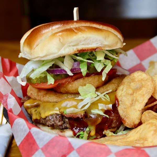 A towering Beckett's Burger Bar burger with onion rings, cheese, and vegetables, served with chips.
