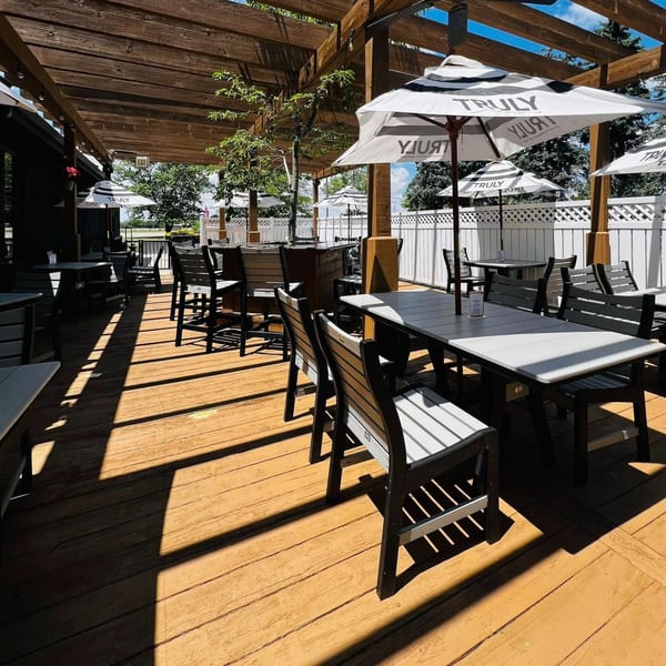 Sunny outdoor patio at Beckett's Burger Bar with wooden pergola, tables, chairs, and Truly umbrellas.