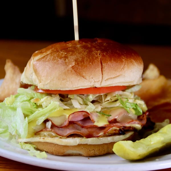 Beckett's Burger Bar's burger with ham, cheese, lettuce, tomato, and a pickle spear.