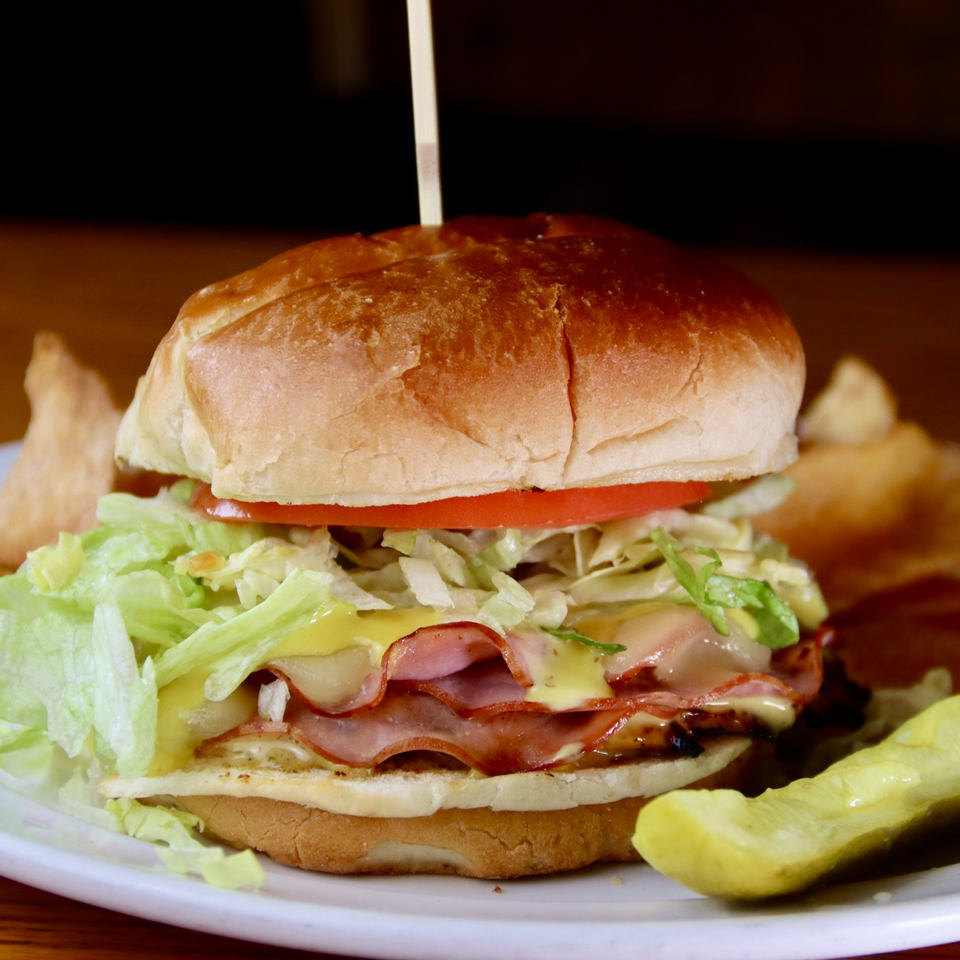 Beckett's Burger Bar's burger with ham, cheese, lettuce, tomato, and a pickle spear.
