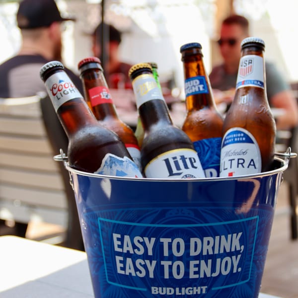 A blue Bud Light bucket filled with various beer bottles, including Coors Light, Miller Lite, and Michelob Ultra.