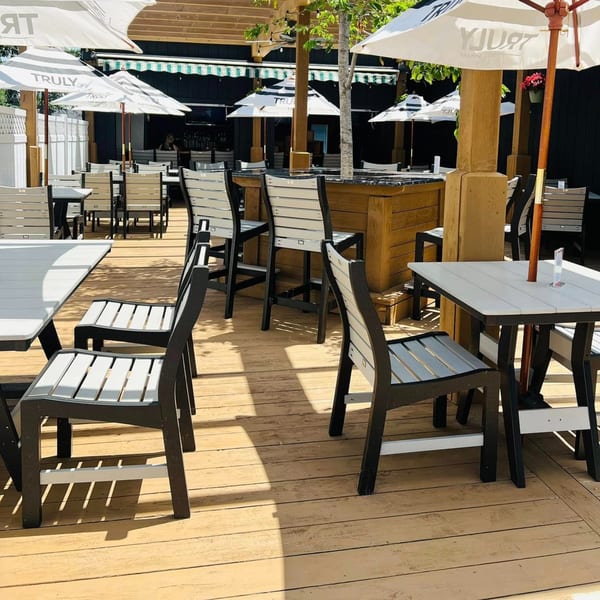 Outdoor patio at Beckett's Burger Bar with empty tables, chairs, and white umbrellas on a wooden deck.