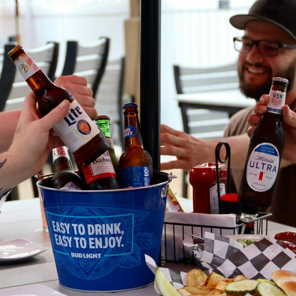 Friends clinking beer bottles from a Bud Light bucket on an outdoor patio table.