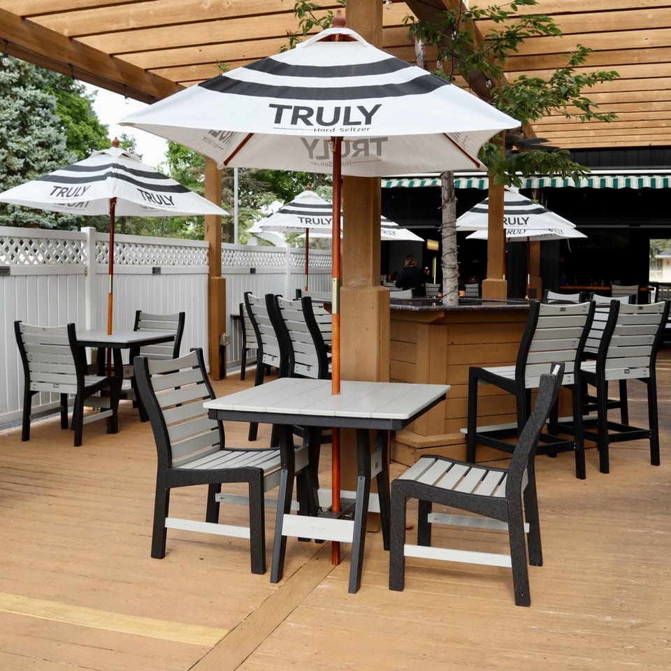 Outdoor patio with wooden deck, black and white striped umbrellas, and gray and black tables and chairs.