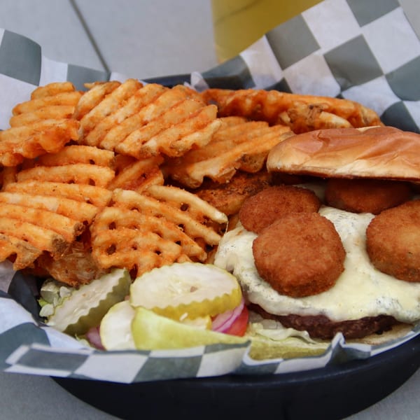A Beckett's Burger Bar burger with white cheese, fried toppings, waffle fries, and pickles.