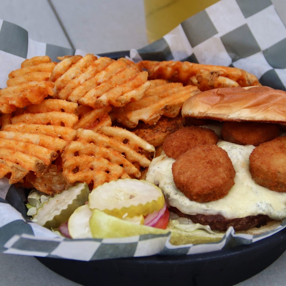 A Beckett's Burger Bar burger with white cheese, fried toppings, waffle fries, and pickles.