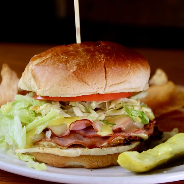 Beckett's Burger Bar's burger with ham, cheese, lettuce, and tomato, served with a pickle.